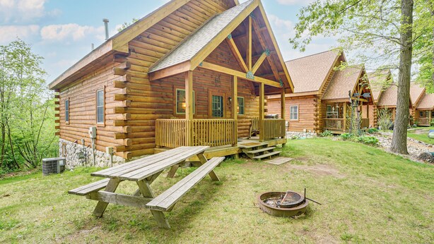 Une cabane en rondins avec une véranda, une table de pique-nique et un foyer.
