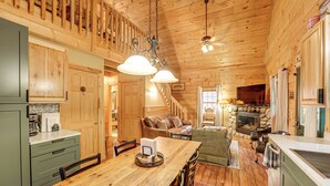 L’intérieur chaleureux d’un chalet avec une table à manger en bois, un coin cuisine et une cheminée.