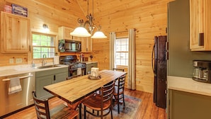 Une cuisine rustique aménagée dans une cabane en bois, avec une table à manger en bois, des chaises, un réfrigérateur, une cuisinière et un four à micro-ondes.