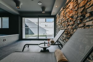 Un espacio moderno de relajación con una pared de piedra, una silla de descanso, una mesita con una vela y vistas a un edificio.