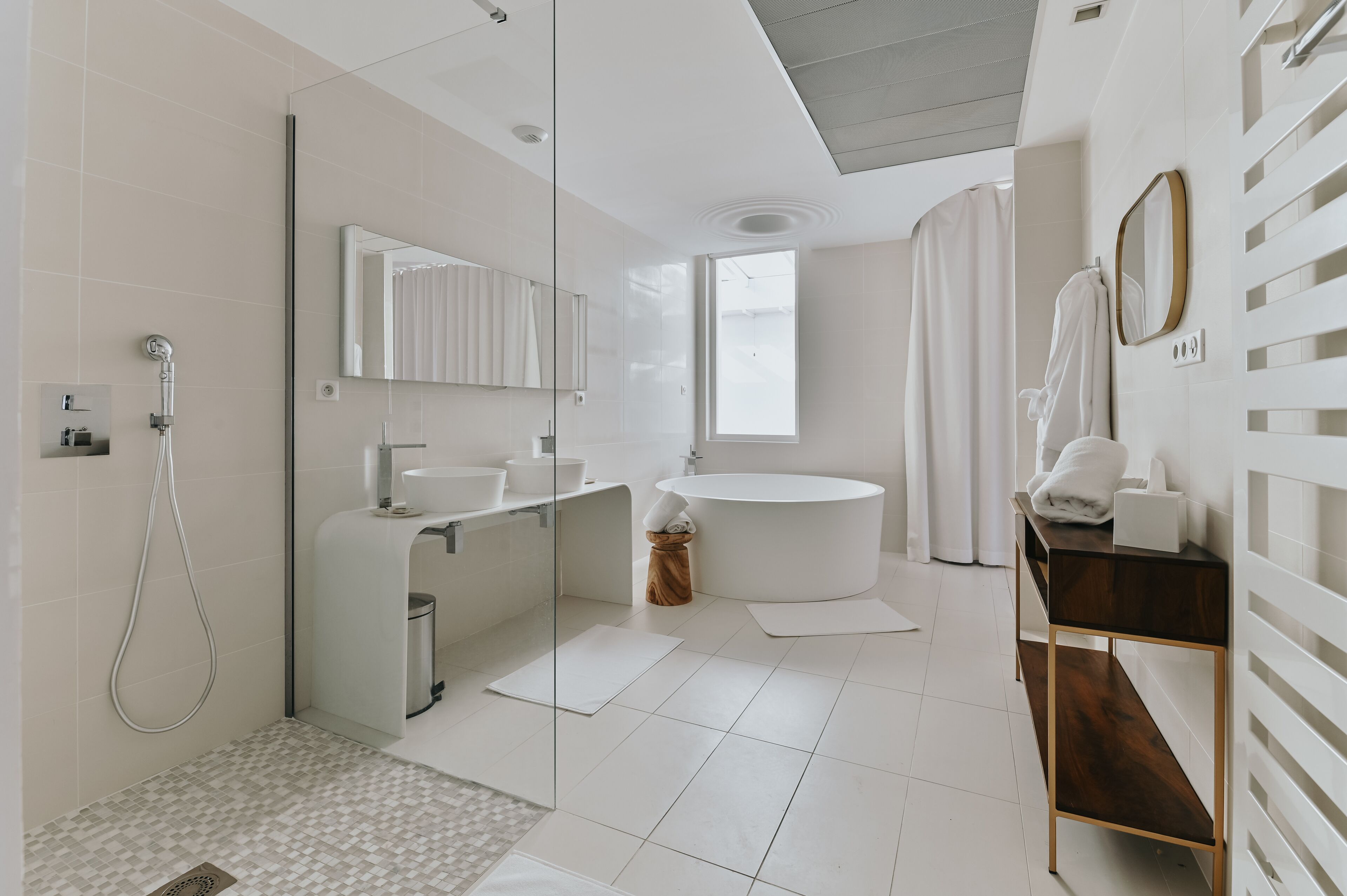 A modern bathroom with a glass shower enclosure, a freestanding bathtub, a round sink, and a vanity with a mirror.
