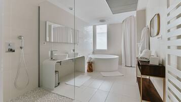 A modern bathroom with a glass shower enclosure, a freestanding bathtub, a round sink, and a vanity with a mirror.