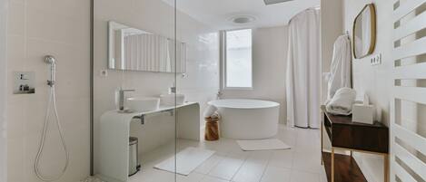 A modern bathroom with a glass shower enclosure, a freestanding bathtub, a round sink, and a vanity with a mirror.