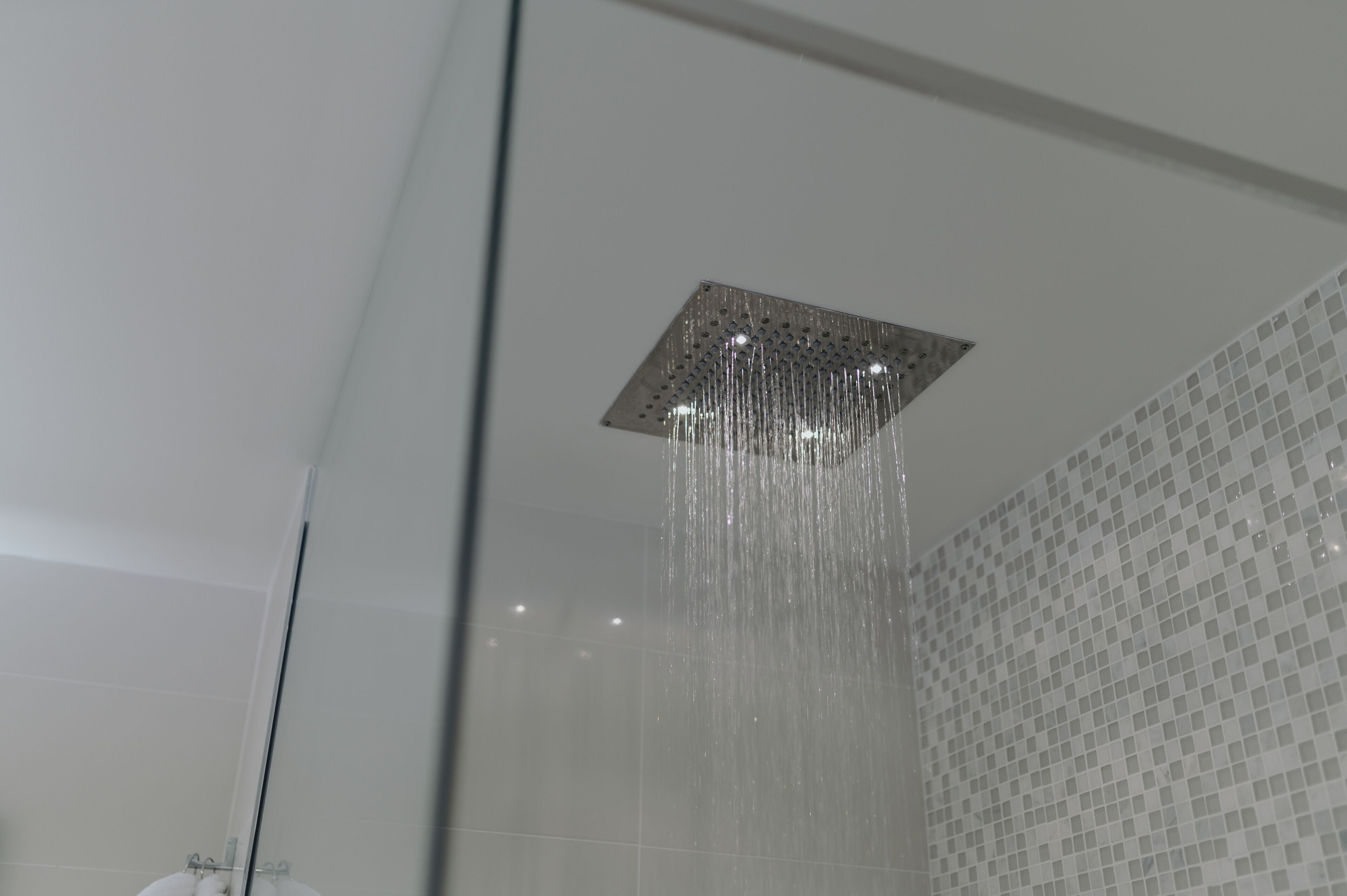 A showerhead with water flowing down in a modern bathroom with tiled walls.