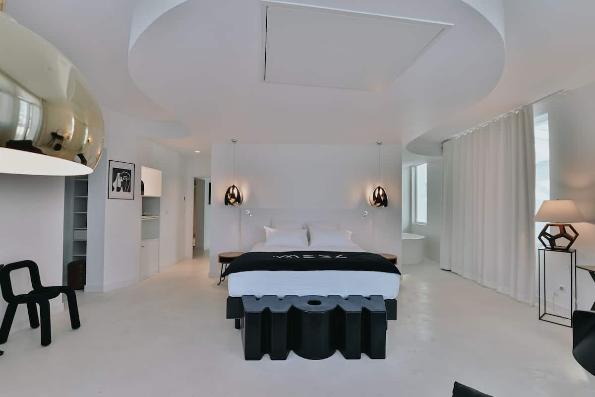 A modern bedroom with a large bed, bedside tables, a chair, a wardrobe, and a mirror.