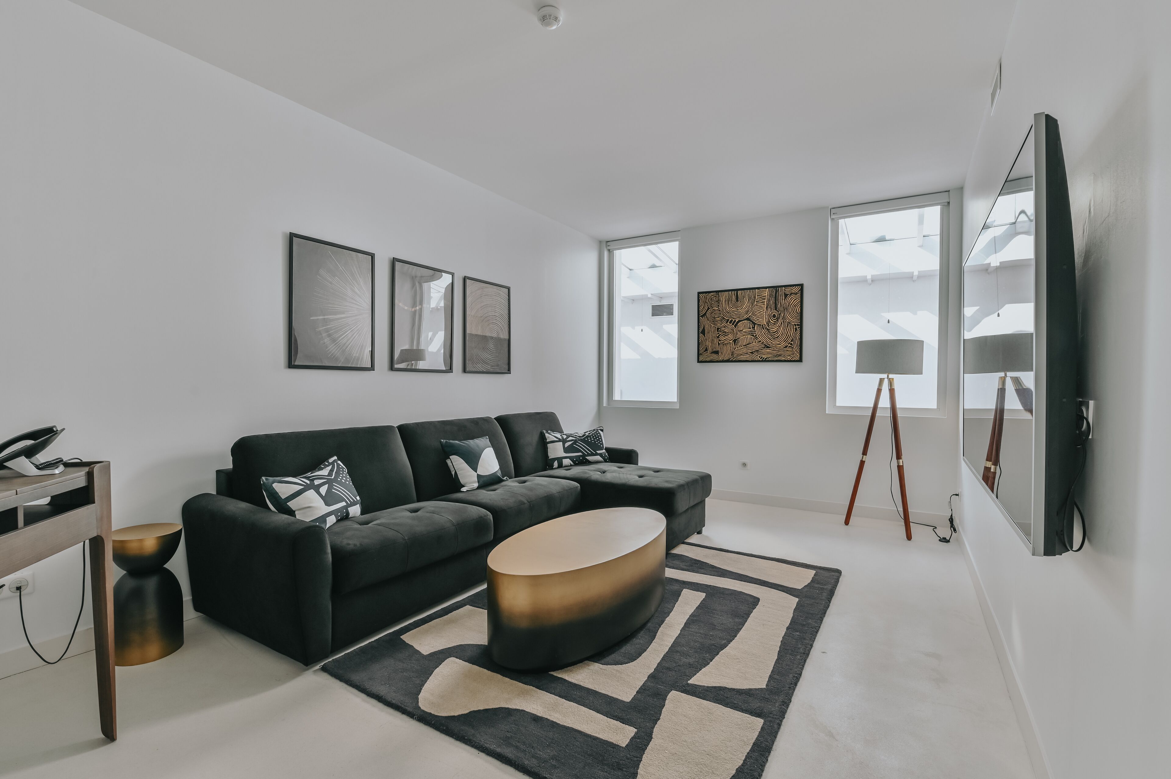A modern living room with a black sectional sofa, a round coffee table, and a large flat-screen TV mounted on the wall.