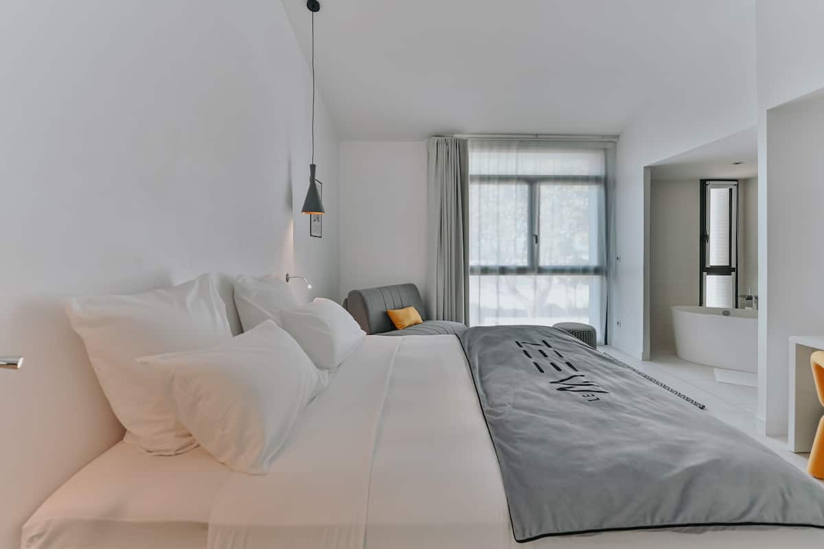 A modern bedroom with a large bed, a chair, a desk, and a window with curtains.