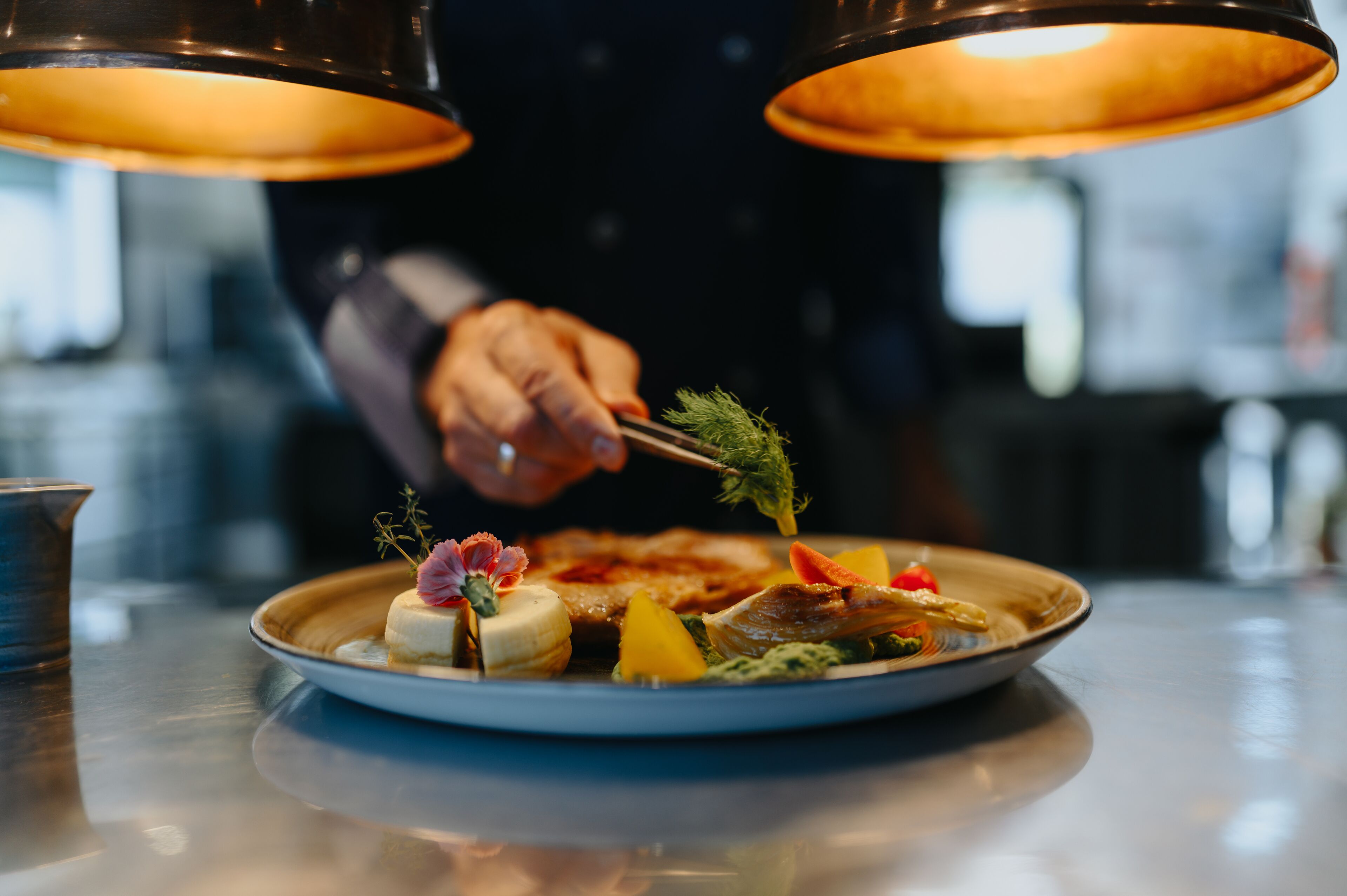 A plate of food with various garnishes and a person using tongs to handle the food.