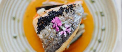 Un plato con pescado, salsa de naranja y flores rosadas.