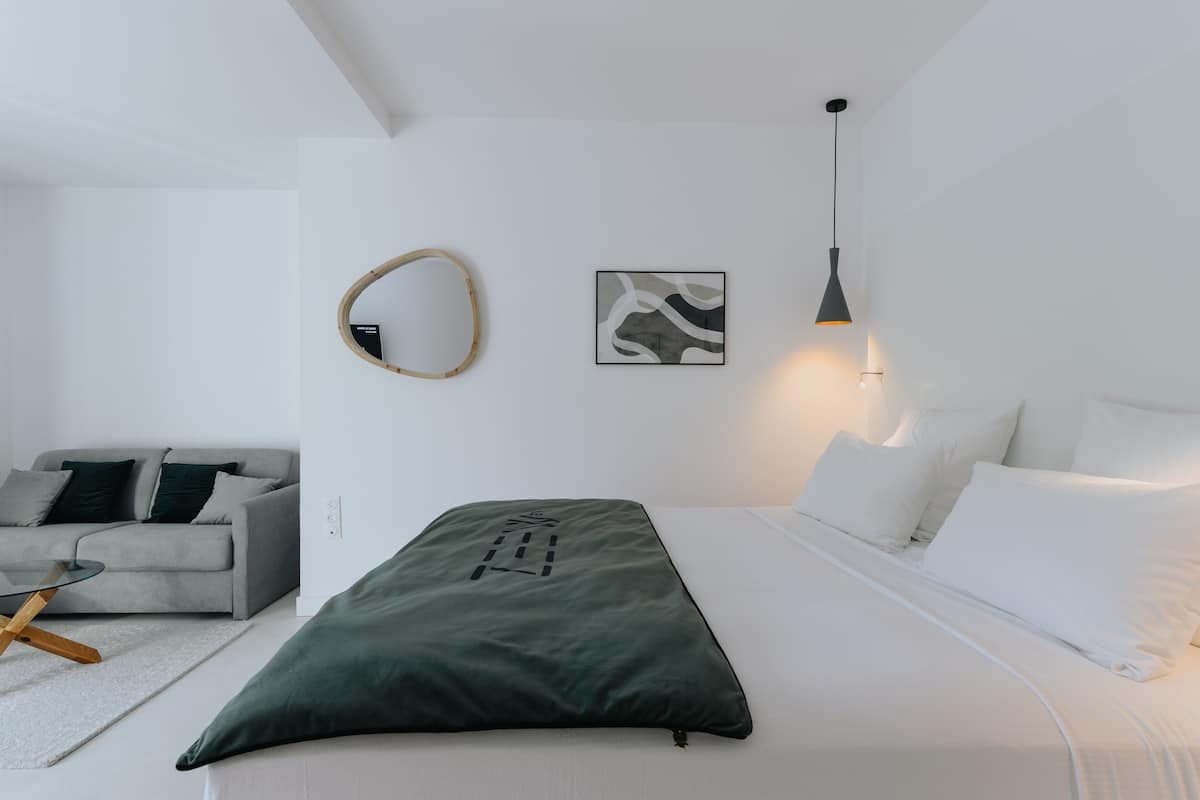 A modern bedroom with a bed, a sofa, a coffee table, a mirror, and wall art.