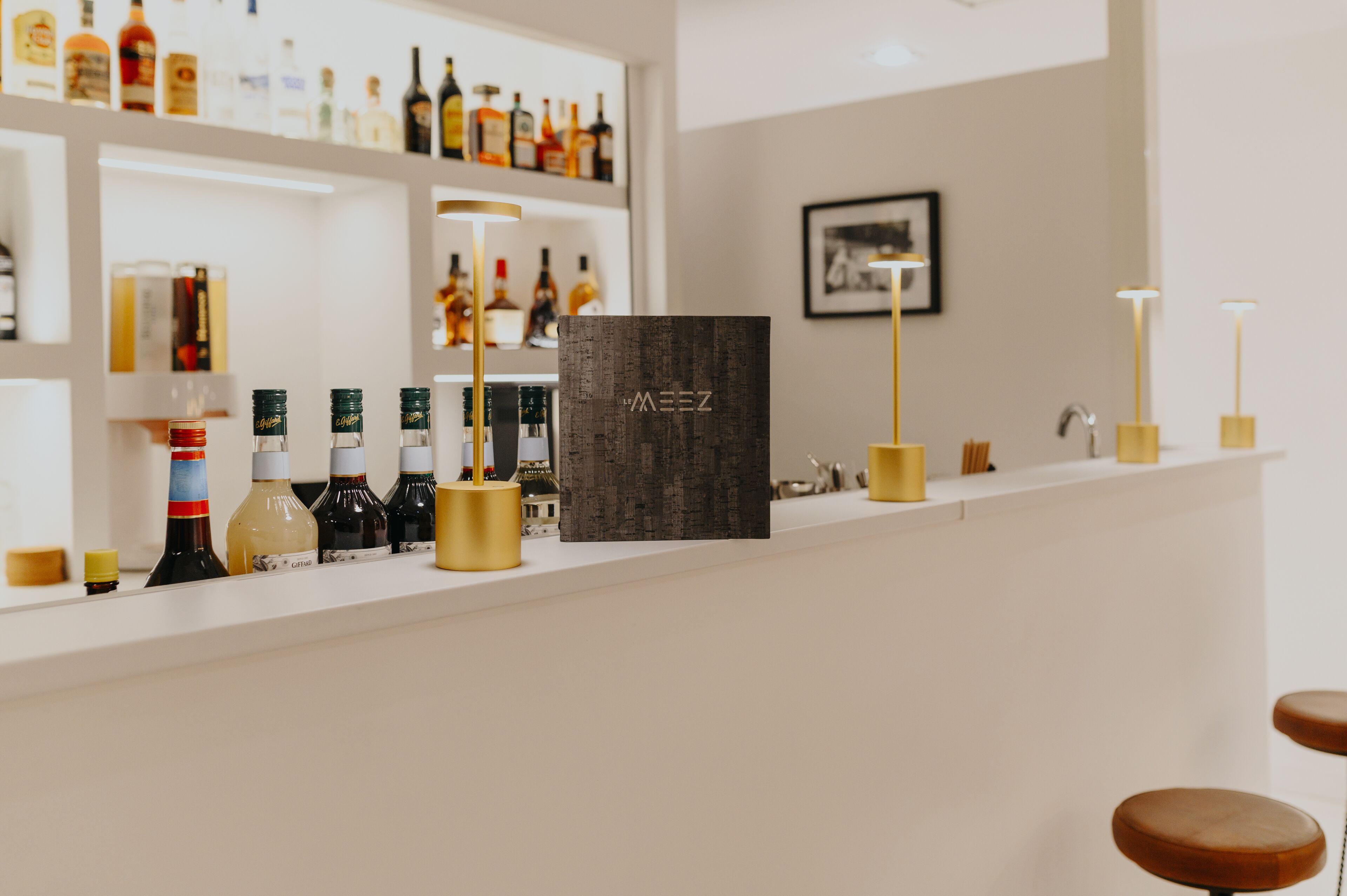 A bar area with shelves of liquor bottles, a framed sign, and bar stools.