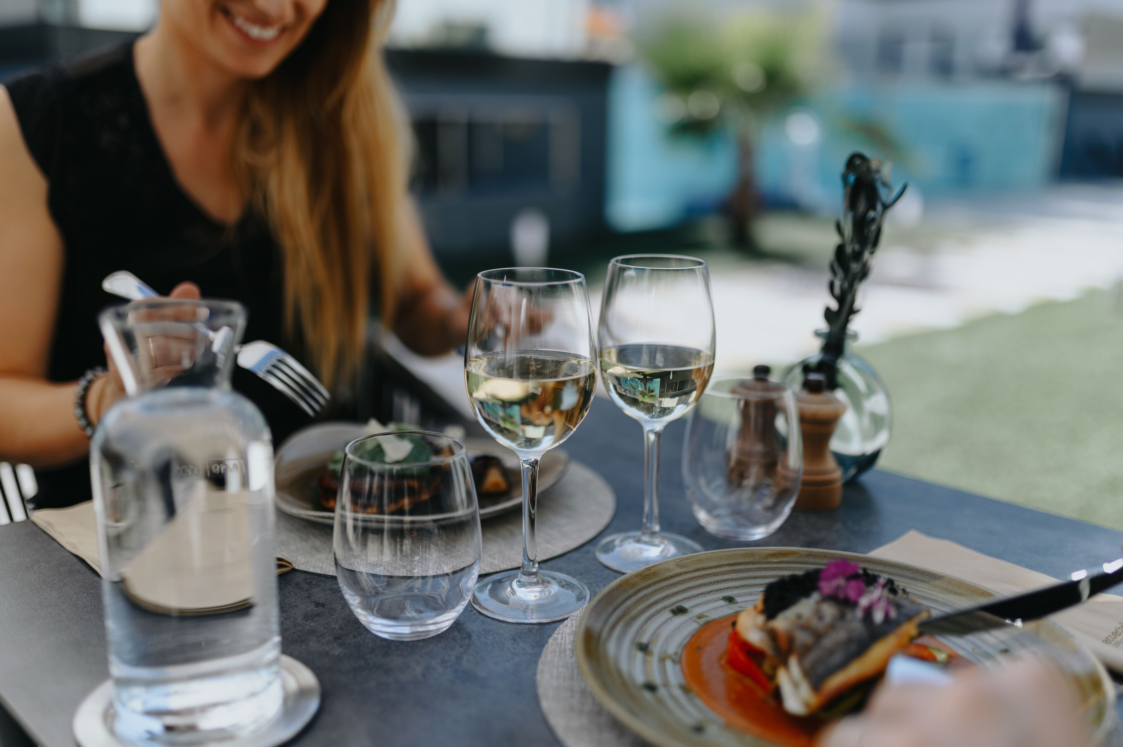 A dining table with a bottle of water, two wine glasses, and a plate with food.