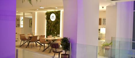 A modern dining area with a round table, chairs, and a wall-mounted logo.