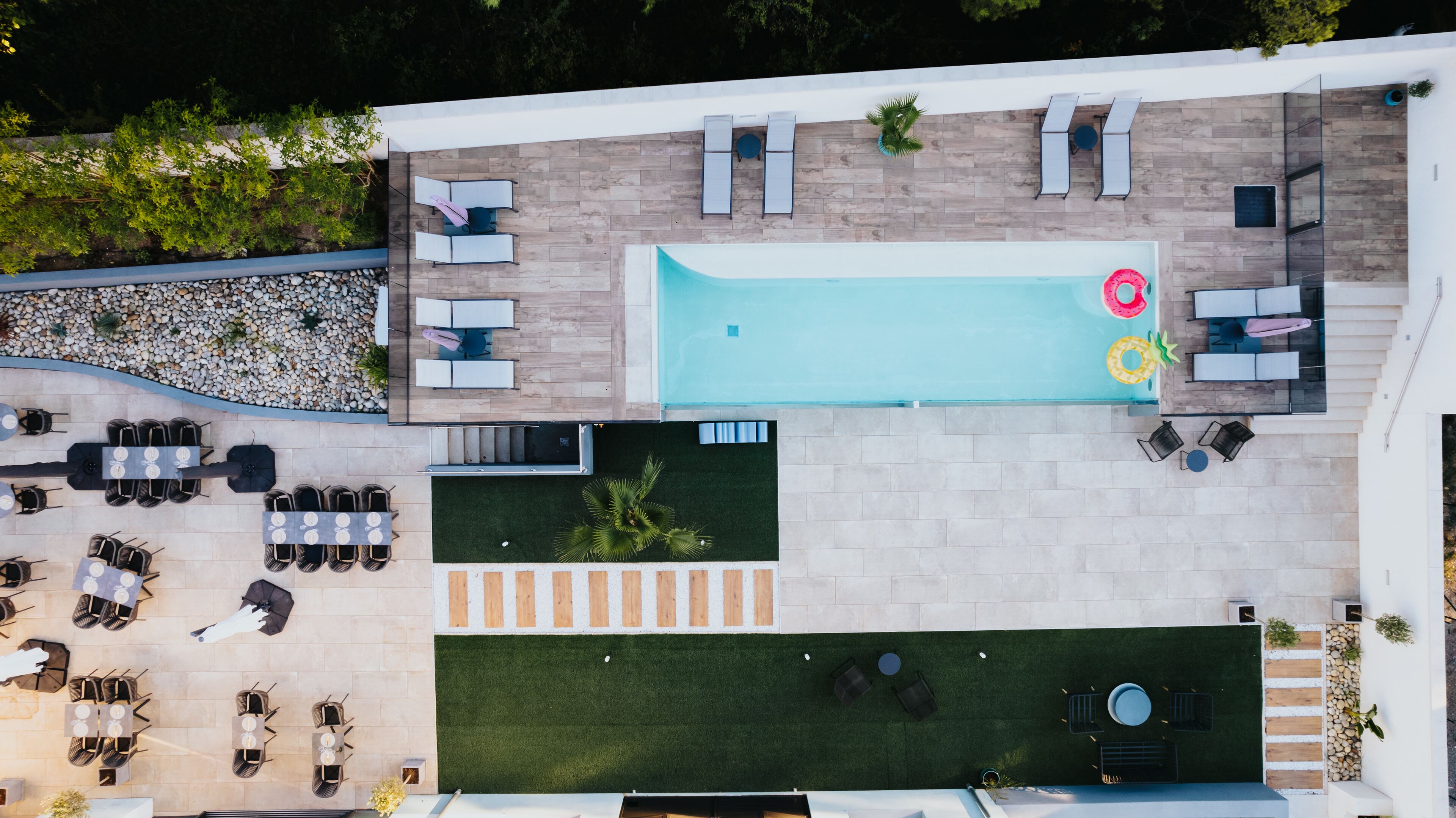 Eine Luftaufnahme eines modernen Außenpoolbereichs mit verschiedenen Sitzgelegenheiten, einem kleinen Pool und einer Rasenfläche.