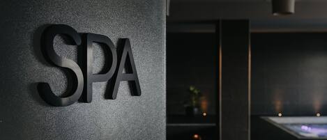 Ein Schild mit den Buchstaben "SPA" an einer strukturierten Wand, das auf einen Wellnessbereich hinweist.