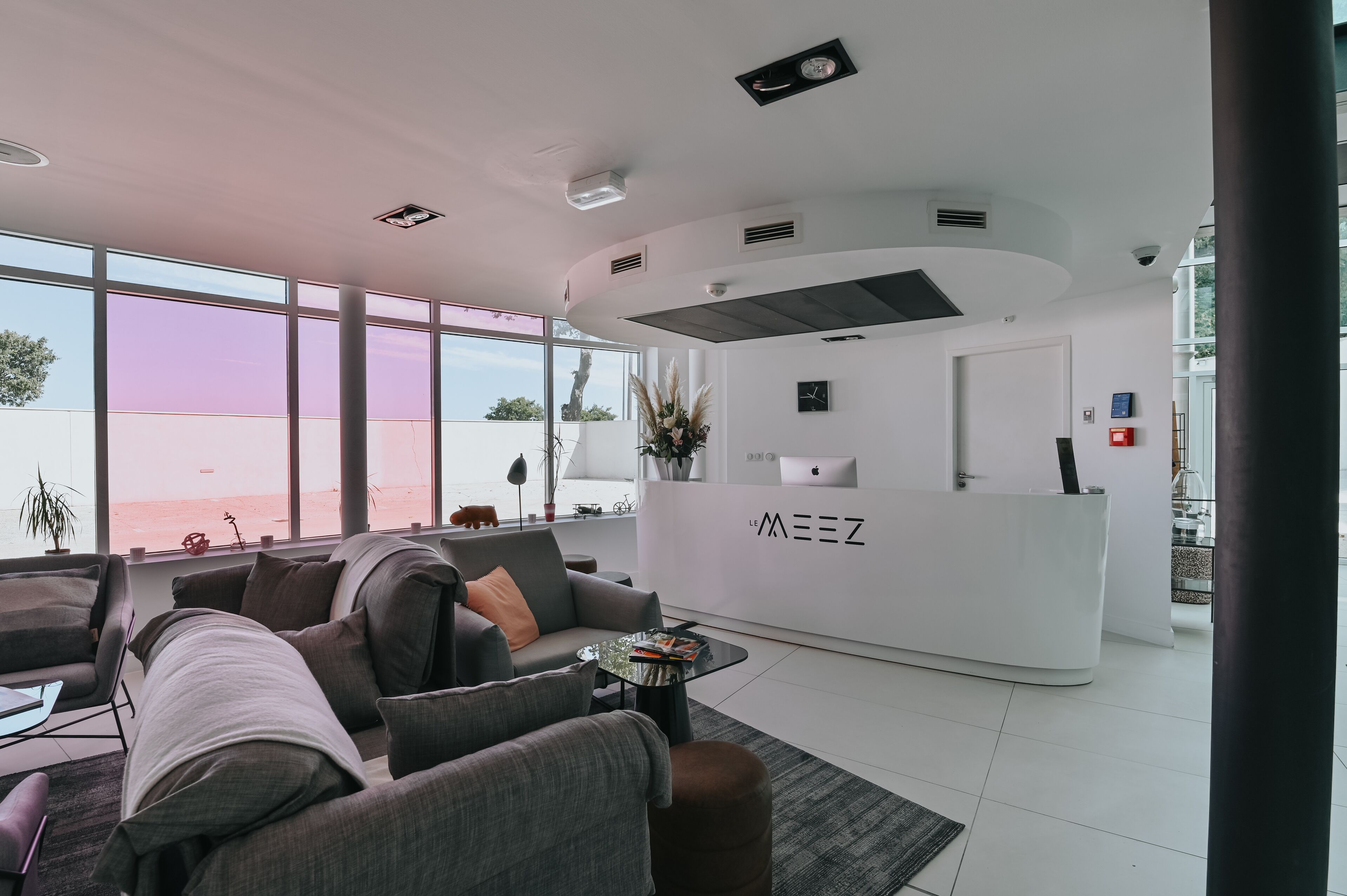 Ein moderner Empfangsbereich mit einem weißen Schreibtisch, grauen Sofas und großen Fenstern mit Blick auf den Strand.