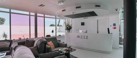Ein moderner Empfangsbereich mit einem weißen Schreibtisch, grauen Sofas und großen Fenstern mit Blick auf den Strand.