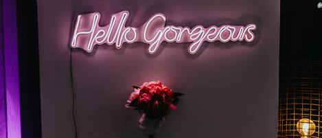 Un letrero de neón con la frase 'Hello Gorgeous' y un ramo de flores sobre una pared.