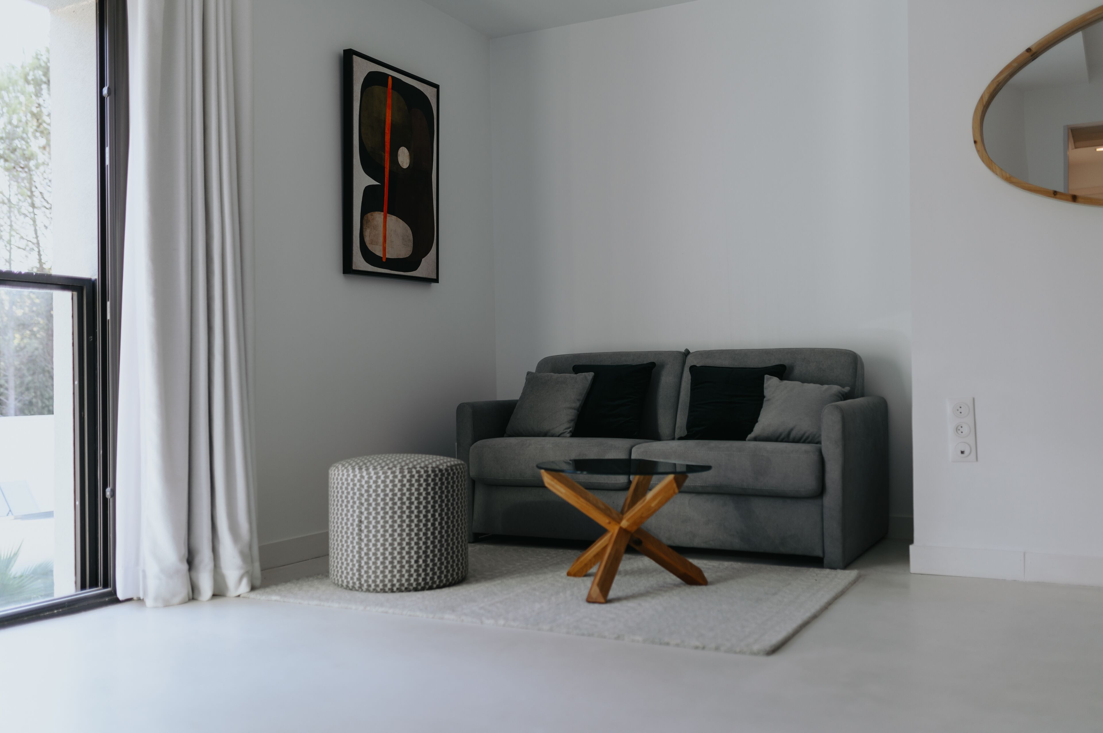 A modern living room with a grey sofa, a round coffee table, and a patterned ottoman.