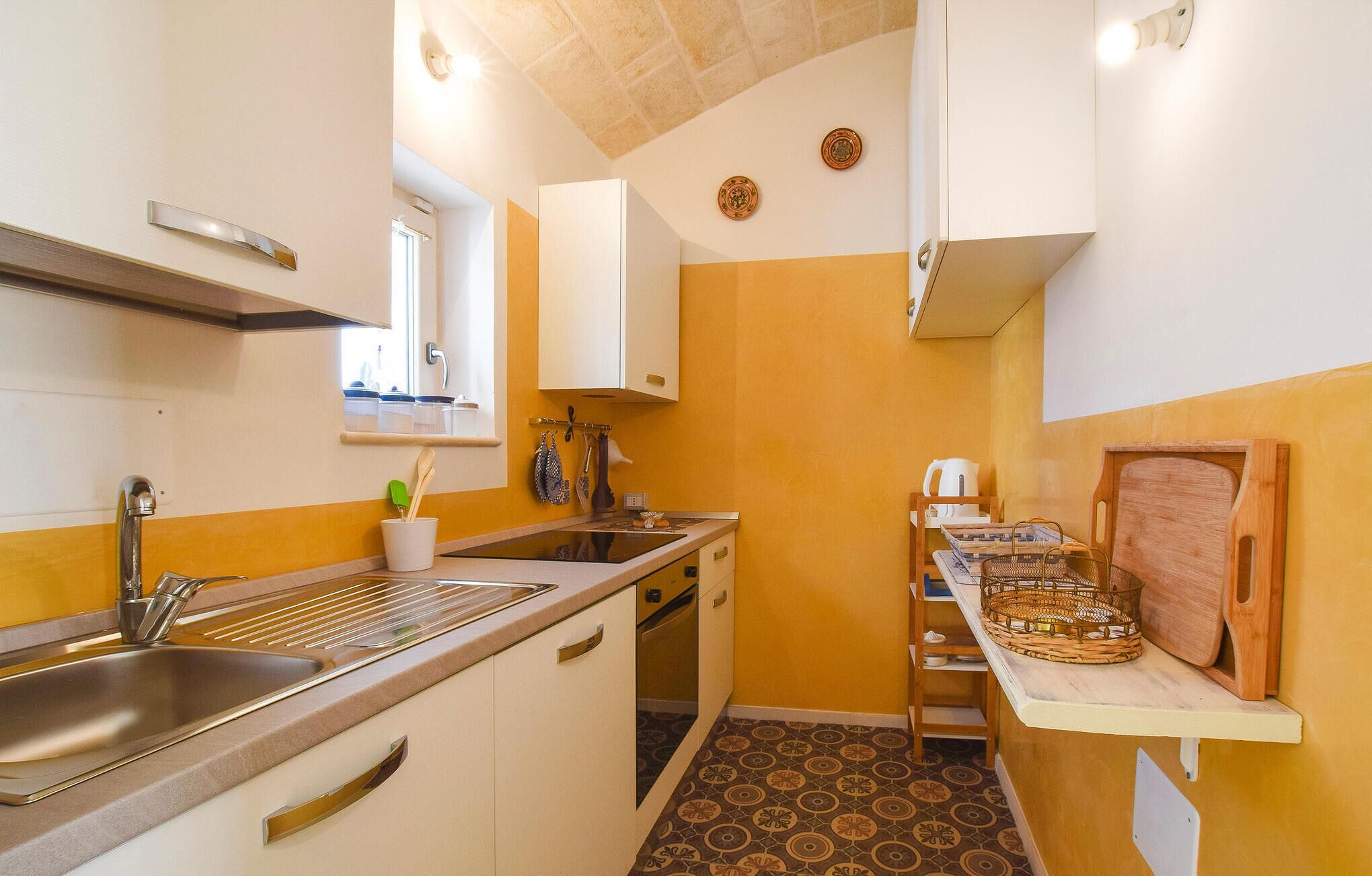 A compact kitchen with a sink, stove, and a small countertop. There is a window above the sink and a door leading to another room.