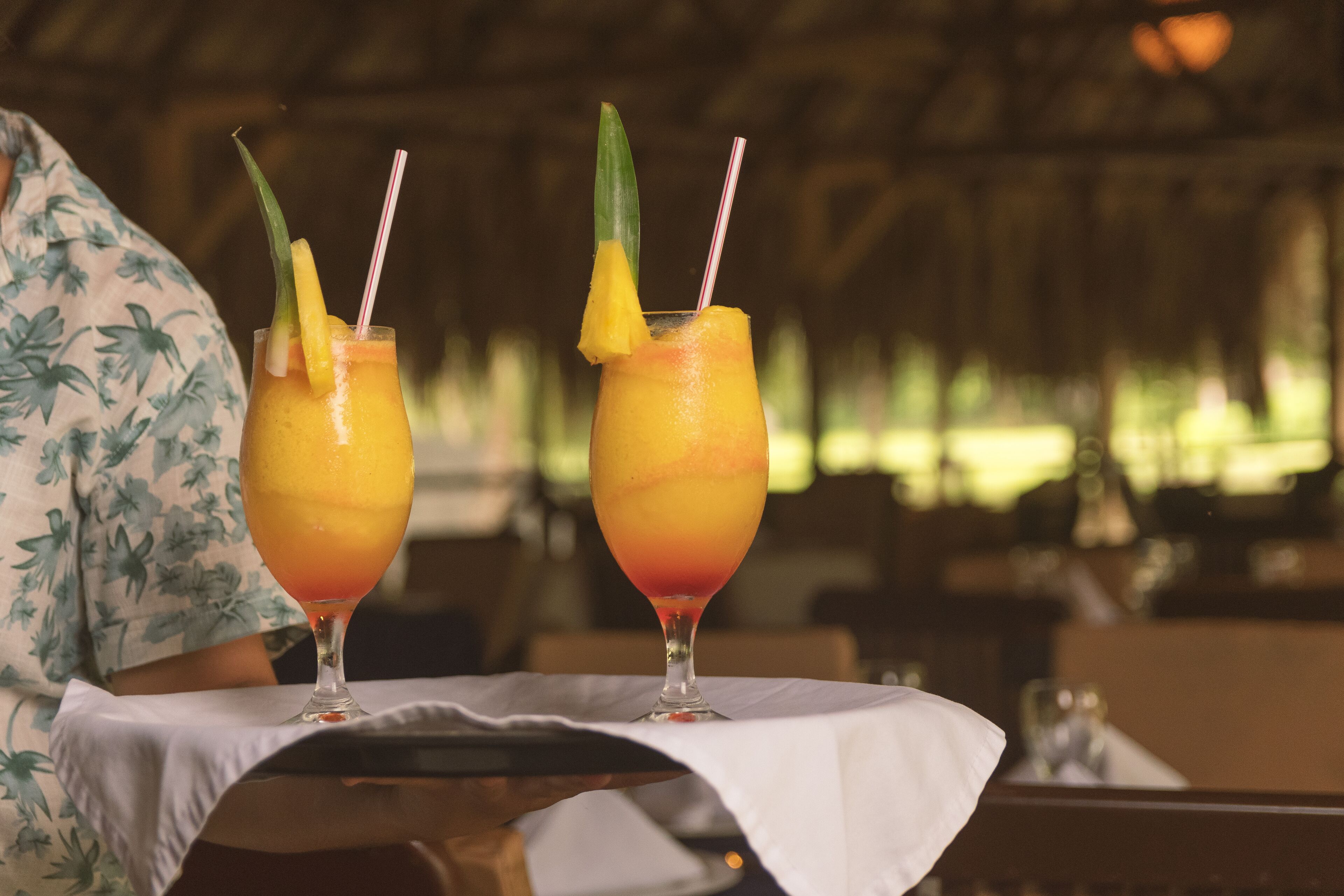 Two drinks with straws and garnishes on a table with a white tablecloth.