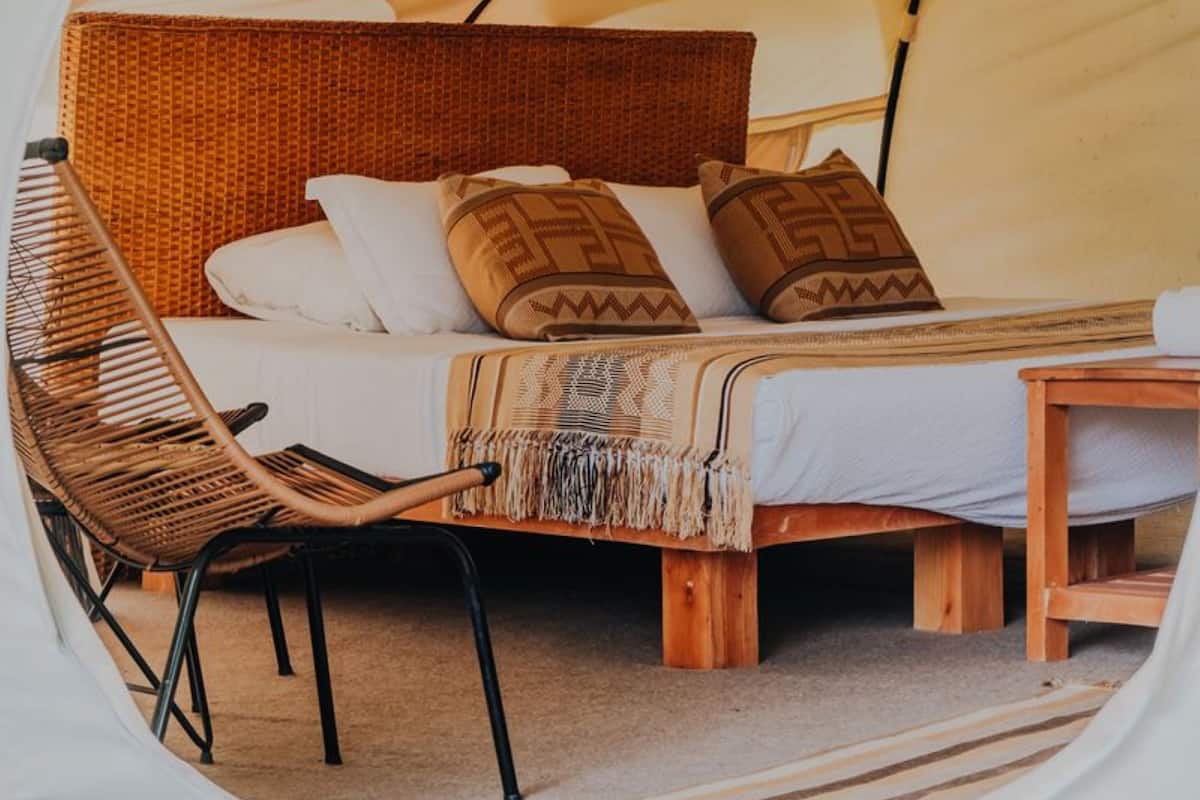 A cozy tented accommodation with a bed, a woven chair, and a small table.