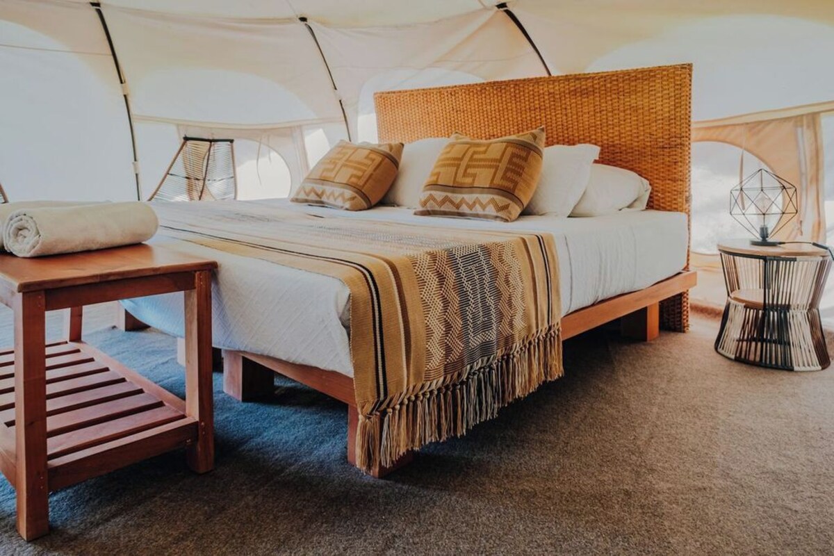 Habitación con tienda de campaña, cama, mesita auxiliar, silla y lámpara.