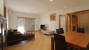 A modern living room with a sofa, a TV, a dining table with chairs, and a sliding door closet.