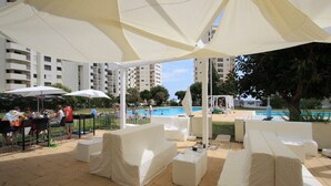 An outdoor patio area with covered seating and a pool in the background.