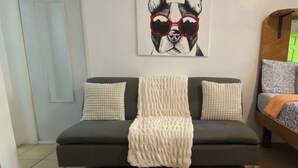 A living room with a dark sofa, a white throw blanket, a wooden coffee table with a dog bowl, and a painting of a dog on the wall. - Turtle Cove 1 King Bed with Pool. Walk to Red Hook (East End)