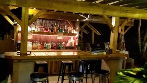 An outdoor bar area with wooden beams, a counter, and stools. - Turtle Cove 1 King Bed with Pool. Walk to Red Hook (East End)