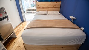 Un dormitorio con cama de madera, ropa de cama blanca, una mesita de noche de madera y una lámpara de mesa pequeña.