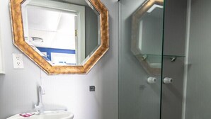 Un baño con un lavabo pedestal, un espejo con marco de madera y un box de ducha de vidrio.