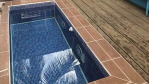 Una casa azul con una terraza de madera, una piscina pequeña y una parrilla.