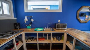 A compact kitchen with a stove, sink, and microwave. There are shelves with dishes and utensils, and a window above the sink. - Moon Apartments  First Floor (#3) (Isla de Utila)