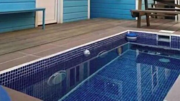 A two-story house with a blue exterior, a front door, and a small pool area with a tiled deck. - Moon Apartments  First Floor (#3) (Isla de Utila)