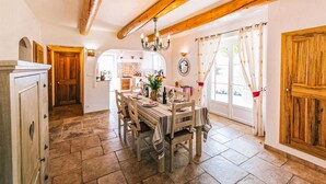 A dining area with a wooden table, chairs, and a chandelier. There is a kitchen visible through an archway. - Amazing home in Lioux (Lioux)