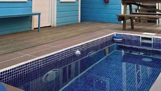 Ein zweistöckiges Haus mit blauer Fassade, einer Haustür und einem kleinen Pool mit Fliesenboden.