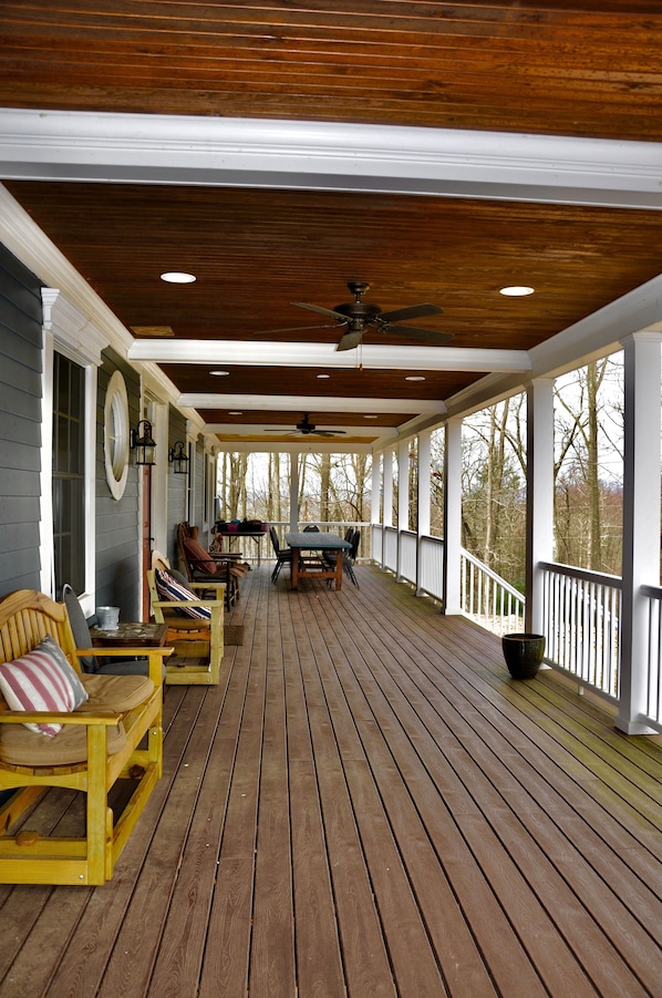 A covered porch with wooden flooring, a table and chairs, and a ceiling fan.
