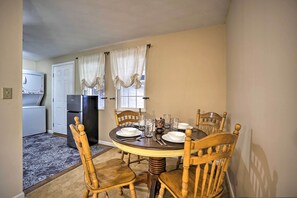 A dining area with a round table, six wooden chairs, and a refrigerator in the background.