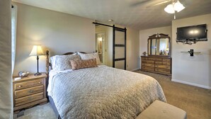 Une chambre à coucher comprenant un lit, une table de chevet, une commode, un miroir, un ventilateur de plafond et un téléviseur.