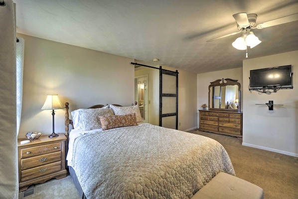 A bedroom with a bed, nightstand, dresser, mirror, ceiling fan, and TV.