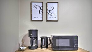 Un comptoir de cuisine avec une machine à café, une bouilloire et un four à micro-ondes. Deux panneaux encadrés sont accrochés au mur, au-dessus du comptoir.
