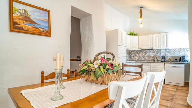 Ein Essbereich mit Holztisch, weißen Stühlen, weißer Tischdecke, Kerzenhalter und einer floralen Dekoration.