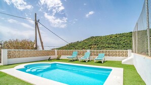 Ein rechteckiger Swimmingpool mit weißem Rand, umgeben von Kunstrasen. Drei Liegestühle mit blau-weißen Streifenpolstern stehen bereit. Eine weiße Zierleiste schließt das Areal ein.