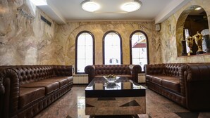 A lobby with a marble wall, a brown leather sofa, a glass coffee table, and a large arched window. - G Hotels (Skopje)