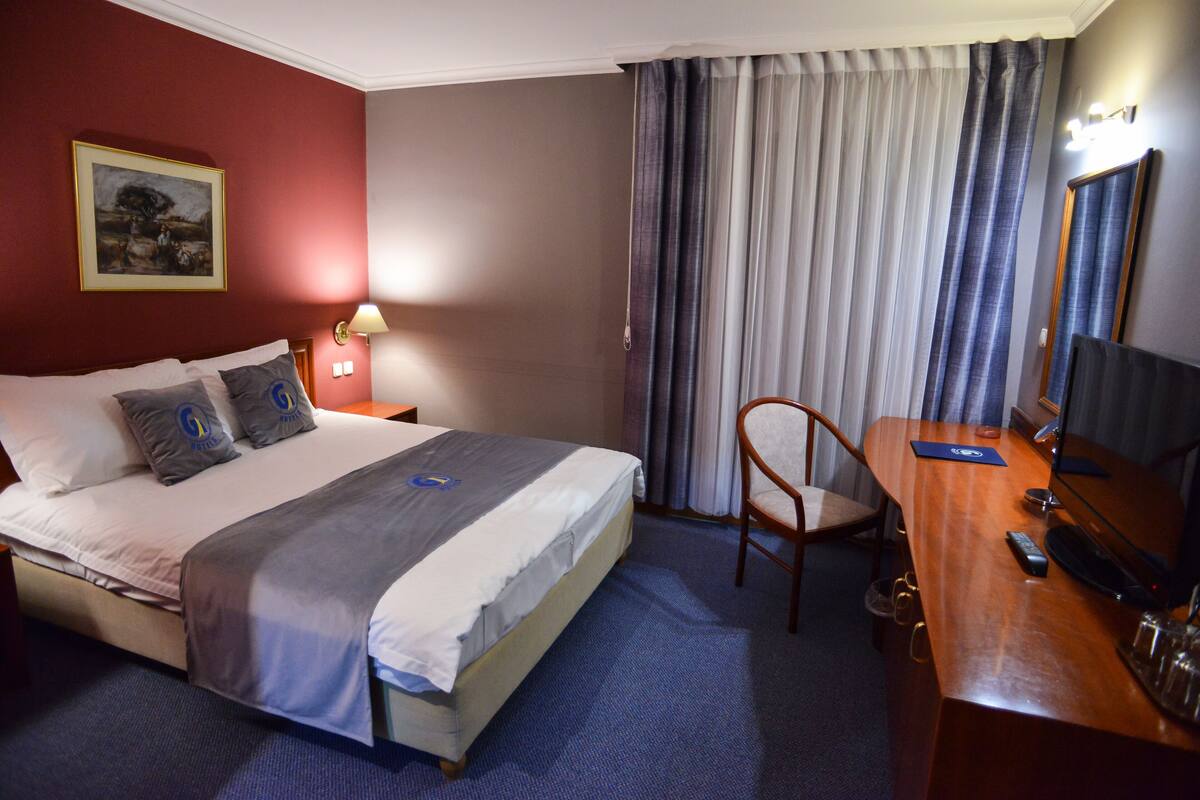 Una habitación de hotel con cama, escritorio, silla, lámpara y un cuadro en la pared.