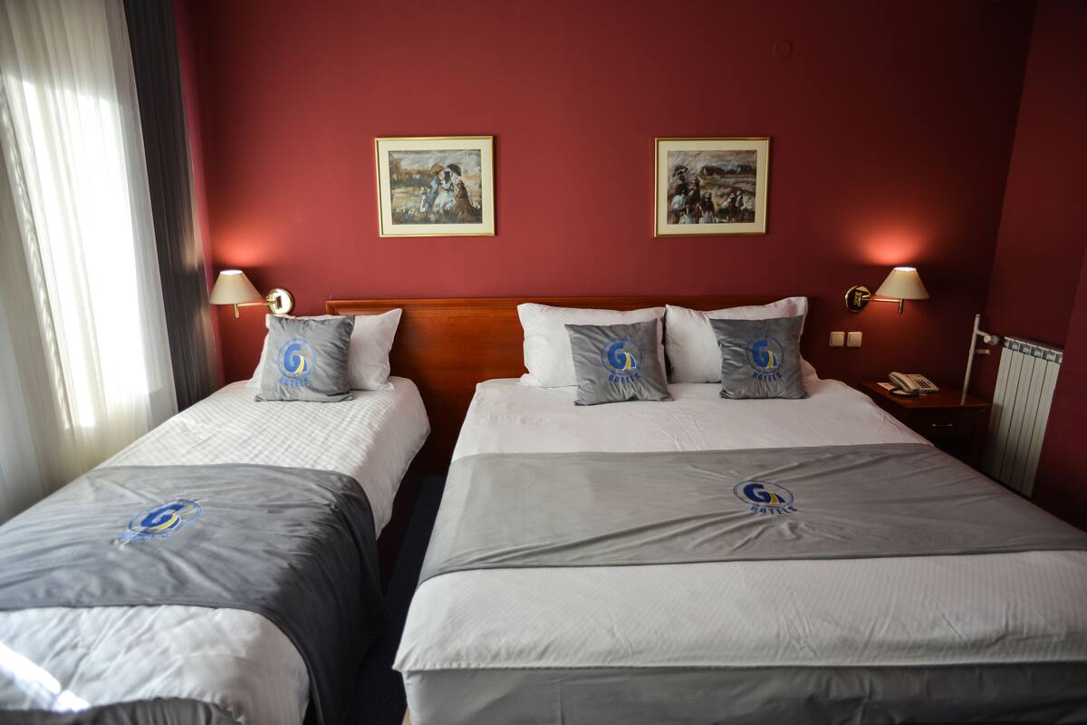 Habitación de hotel con dos camas, cada una con almohadas y un logotipo a juego, cabecera de madera y dos cuadros en la pared.