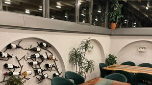 A restaurant interior with green upholstered chairs, wooden tables, and a wall-mounted wine rack. - G Hotels (Skopje)