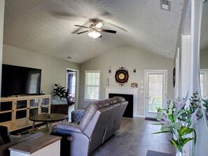 Un salon comprenant un canapé, un téléviseur, un ventilateur de plafond, une cheminée et une plante.